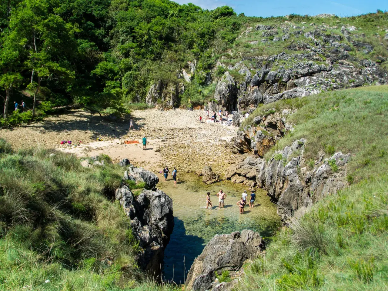 Gente disfrutando del sol y el agua cristalina en la playa de cobijero, rodeada de rocas y vegetación exuberante.