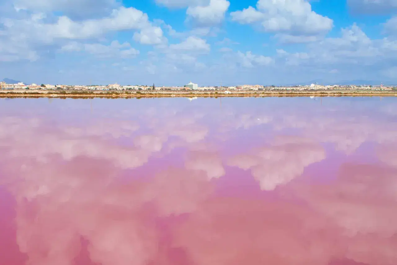 El agua rosa de la playa de Murcia refleja las nubes blancas bajo un cielo azul. Un paisaje surrealista y hermoso.