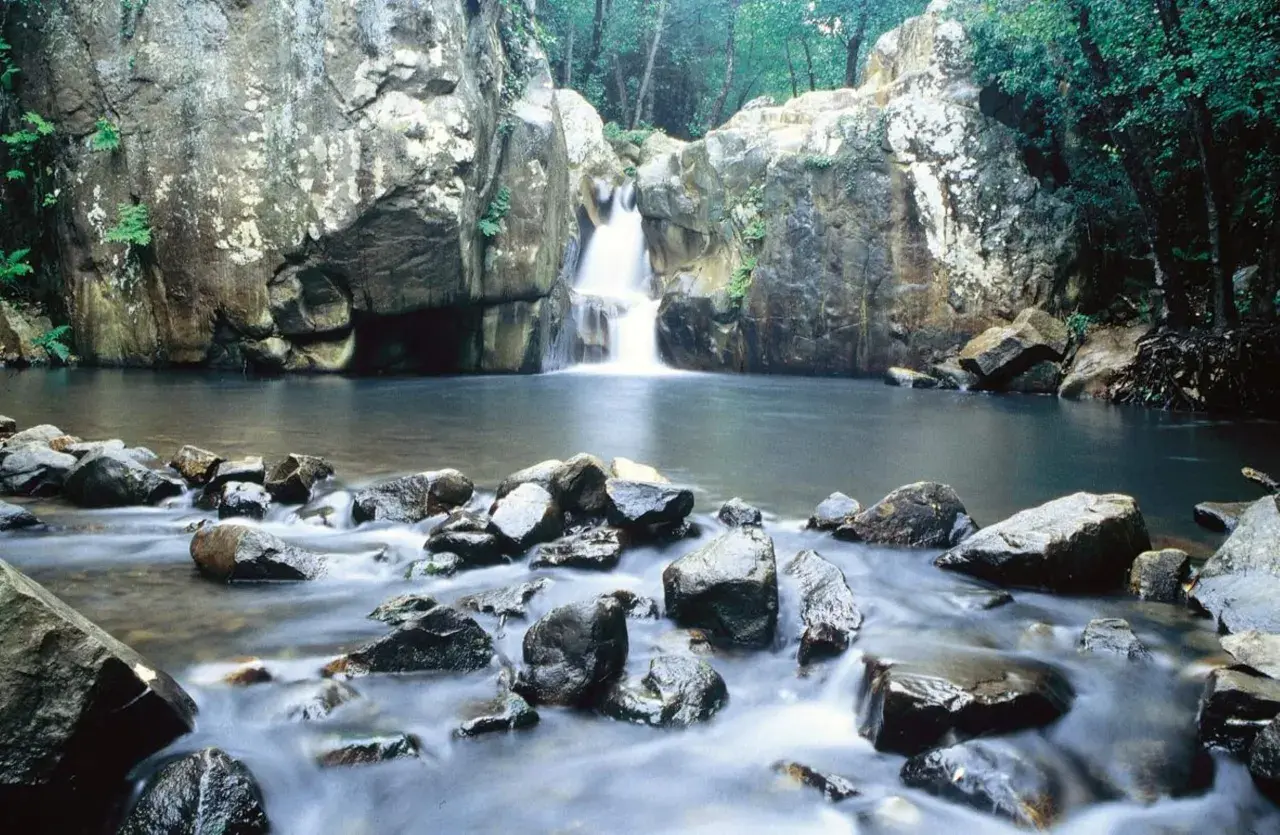 Cascada y río en la ruta del Río de la Miel, rodeado de rocas y vegetación exuberante.