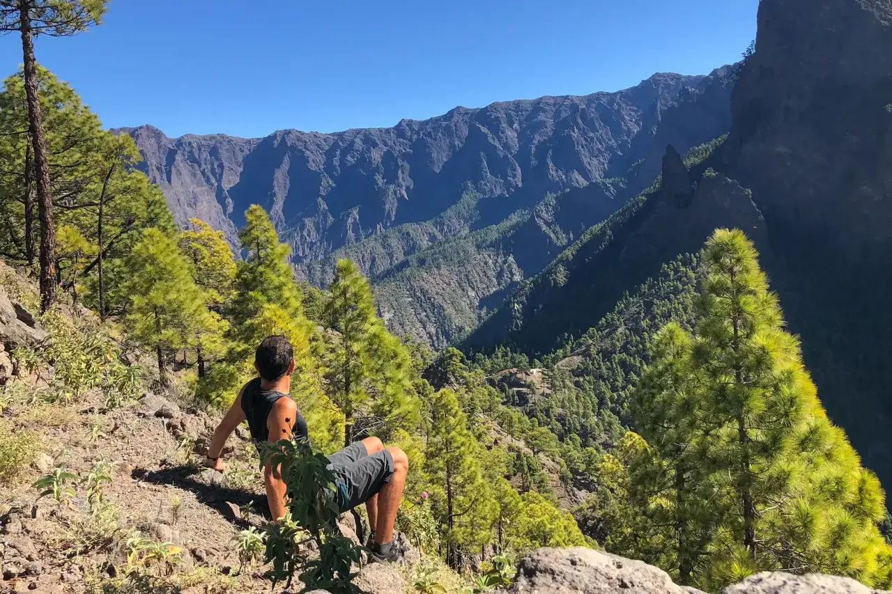 Hombre sentado en la ladera, contemplando el imponente paisaje montañoso del **cubo de la galga**.