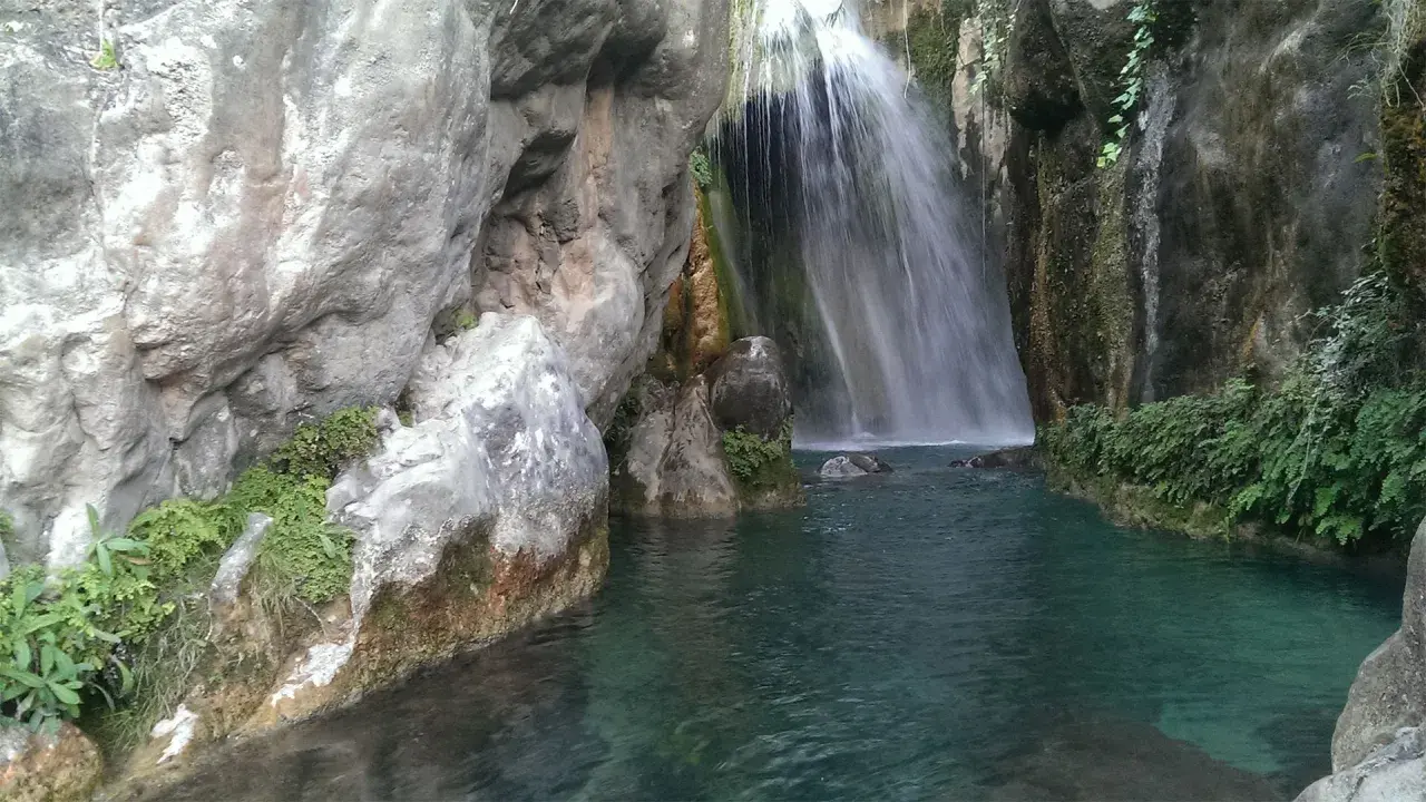 Cascada en las fuentes del Algar, con aguas turquesas y vegetación exuberante entre rocas.