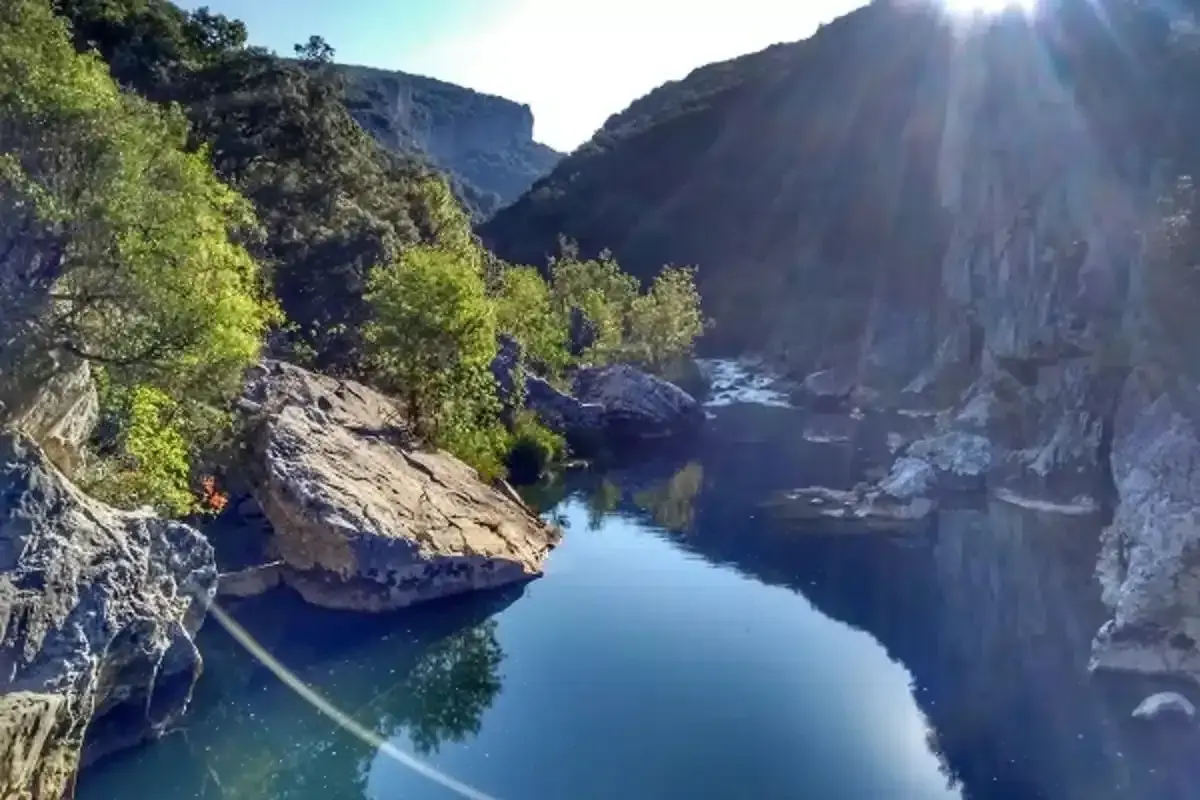 Río sereno en la Foz de Lumbier, un paisaje ideal para una ruta. Rocas y vegetación bordean el agua azul bajo el sol.