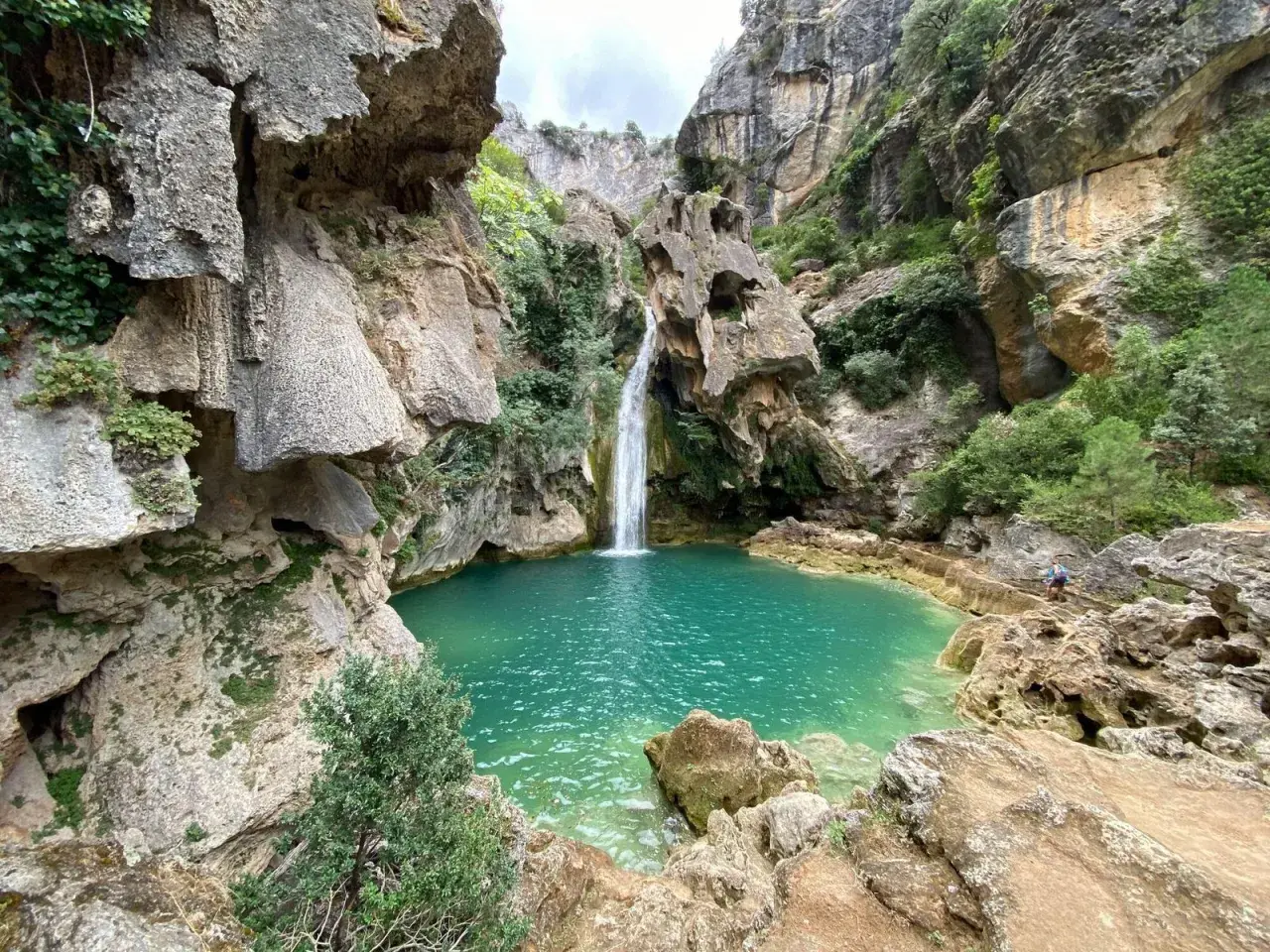 La cascada de la calavera cae en una poza de agua turquesa, rodeada de rocas y vegetación exuberante.
