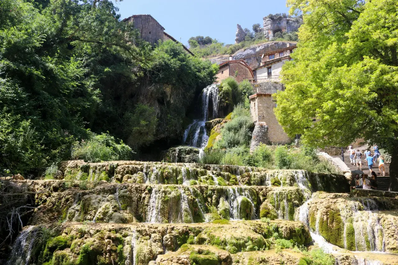 Cascada en las Hoces del Ebro, con casas de piedra integradas en la roca y vegetación exuberante.