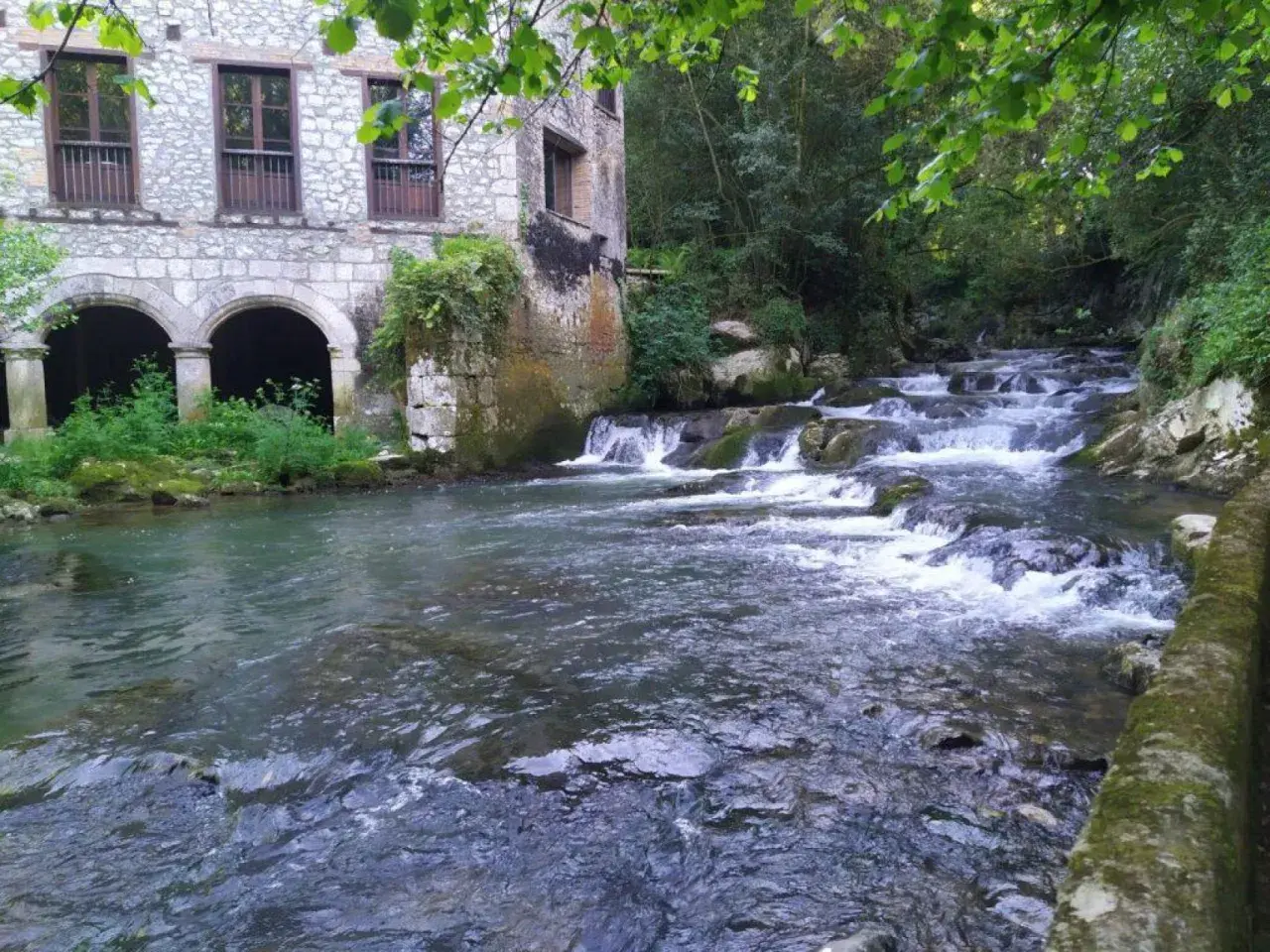 Edificio de piedra con arcos junto a un río con cascadas. Parece la fuente del francés, un lugar idílico.