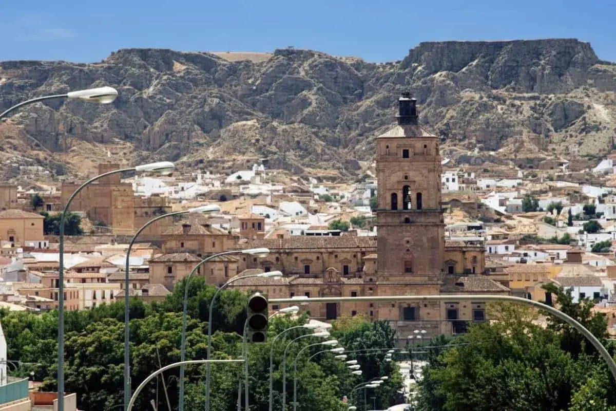 Vista panorámica de Guadix, con su imponente torre campanario y casas blancas al pie de montañas rocosas. Ideal para planificar cómo llegar.