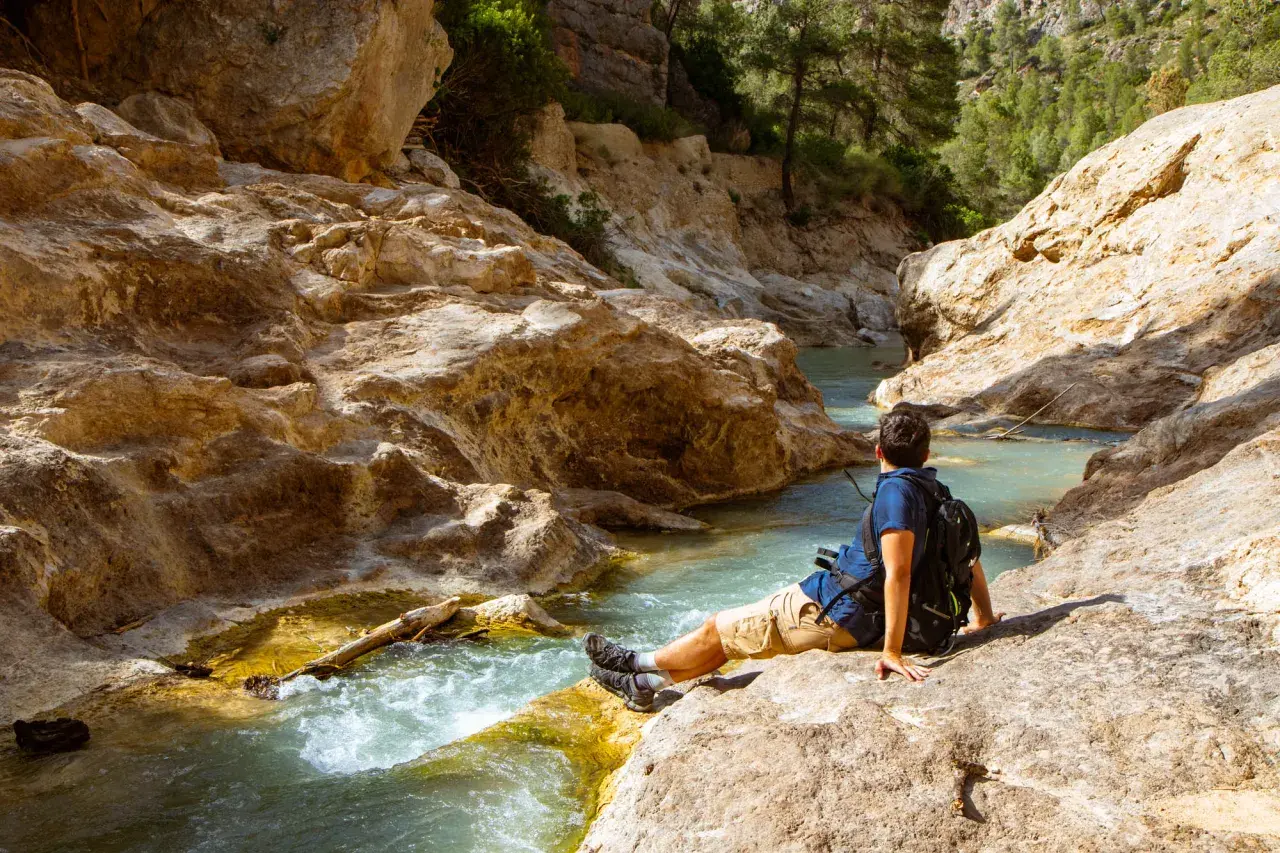 Hombre sentado junto a un río turquesa en un cañón rocoso. Un lugar idílico para explorar, ¡así es como llegar!