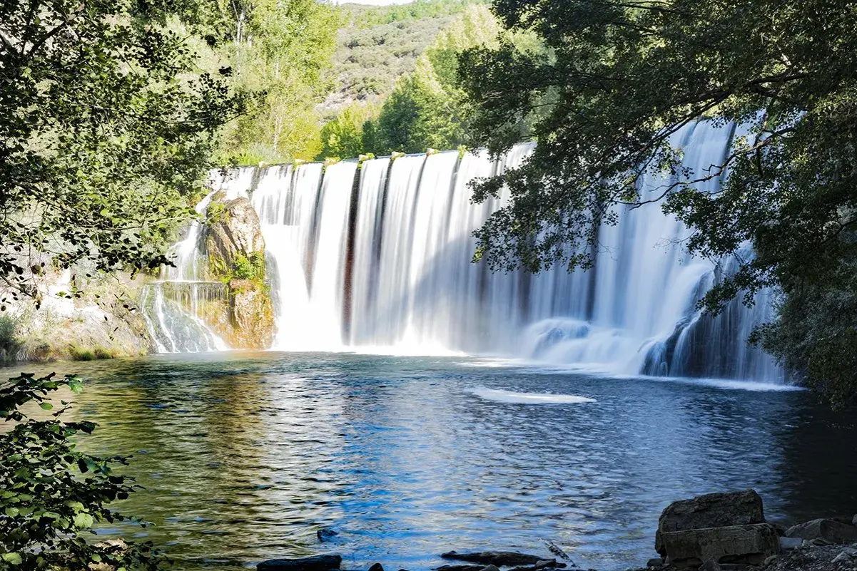 El Salto del Pelgo, una cascada imponente con agua sedosa cayendo sobre rocas, rodeada de vegetación exuberante y un estanque azul profundo.