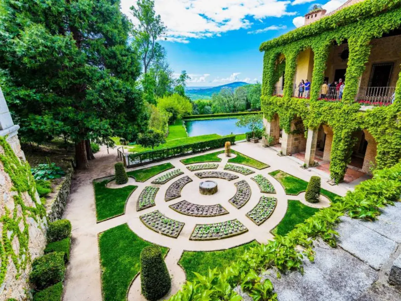 Jardín renacentista con estanque y edificio cubierto de hiedra, evocando la serenidad de los Cuacos de Yuste.