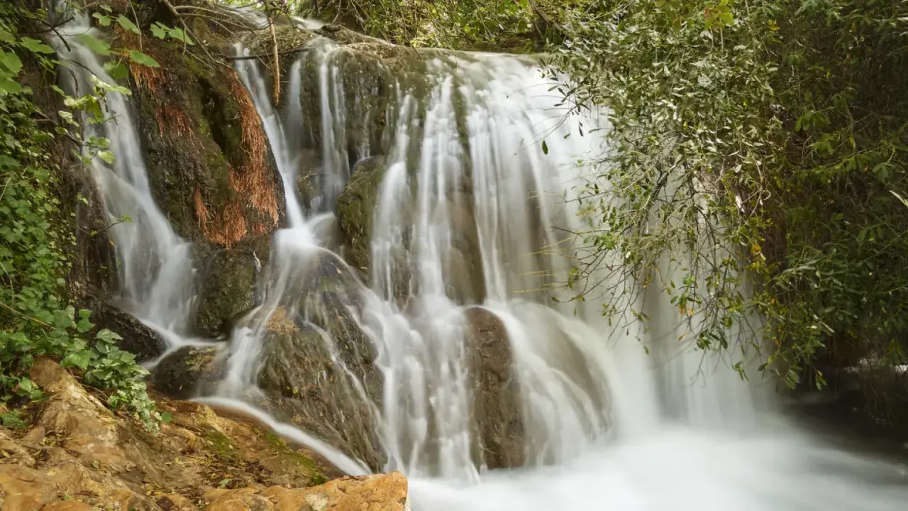 Cascadas de Hueznar, un velo de agua blanca desciende por rocas cubiertas de musgo y vegetación exuberante.