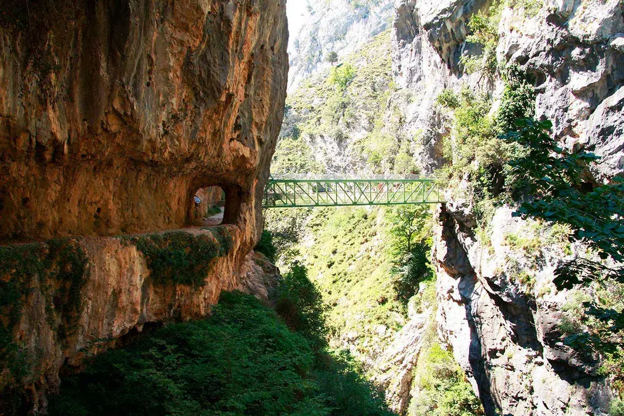 Un puente verde cruza un desfiladero rocoso, parte de la ruta del Cares. El tiempo parece perfecto para esta aventura.