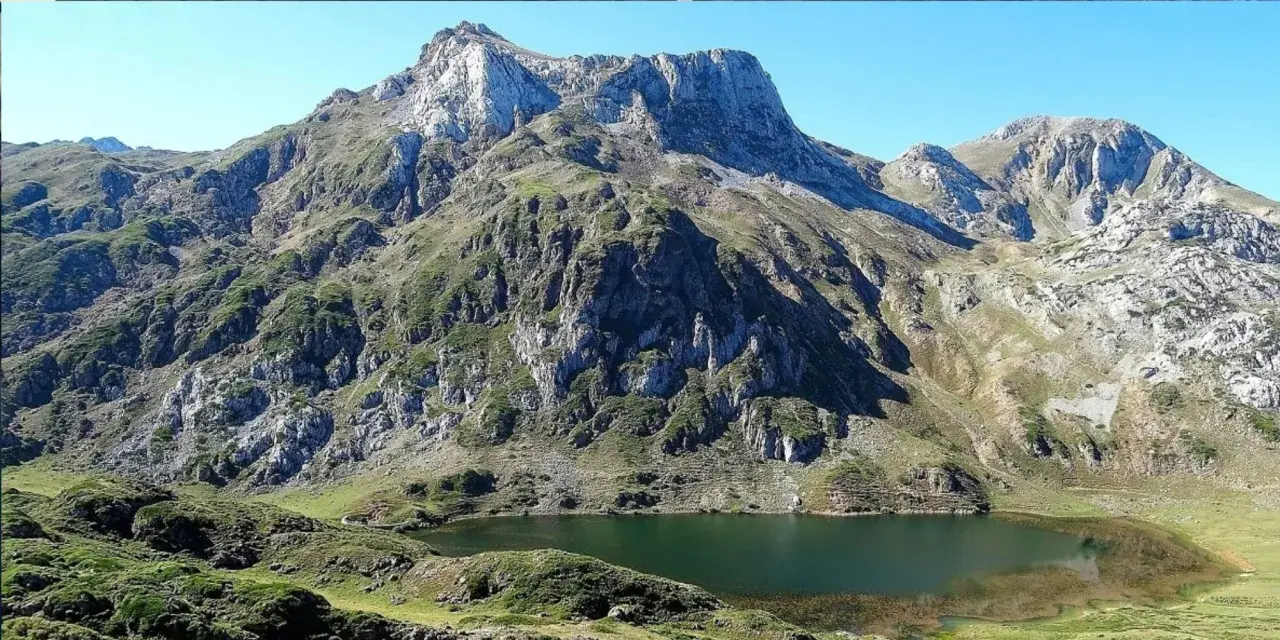 Majestuoso lago en la ruta Lagos de Saliencia, rodeado de imponentes montañas rocosas y vegetación verde.