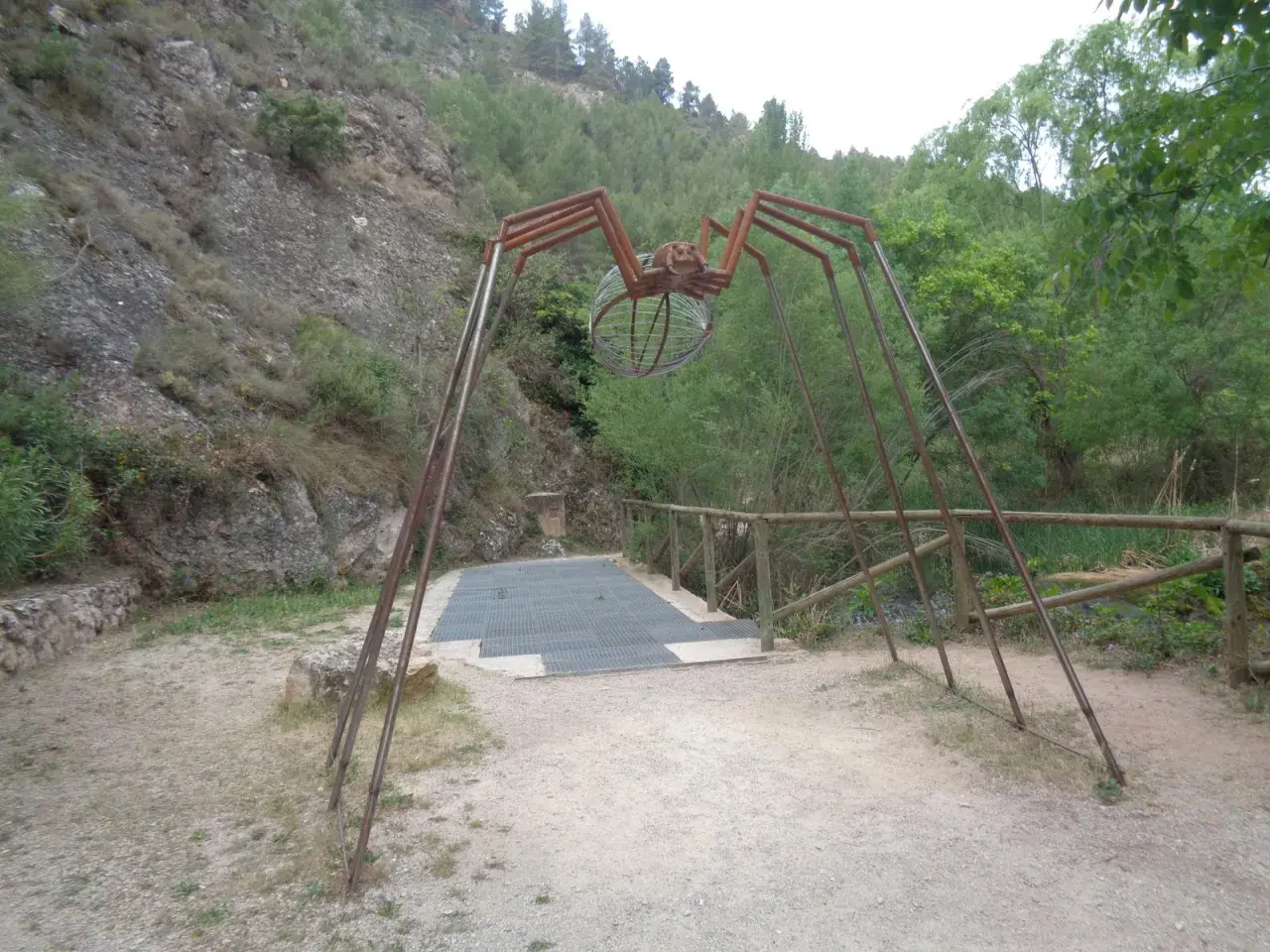 Escultura de araña gigante en la ruta de las esculturas Bogarra, con un cuerpo de alambre y patas metálicas, sobre un camino de grava.