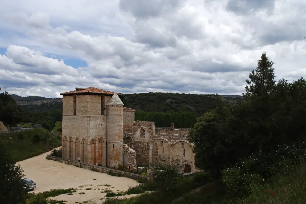 Ruinas del monasterio de San Pedro de Arlanza, con su torre robusta y arcos de piedra bajo un cielo nublado.