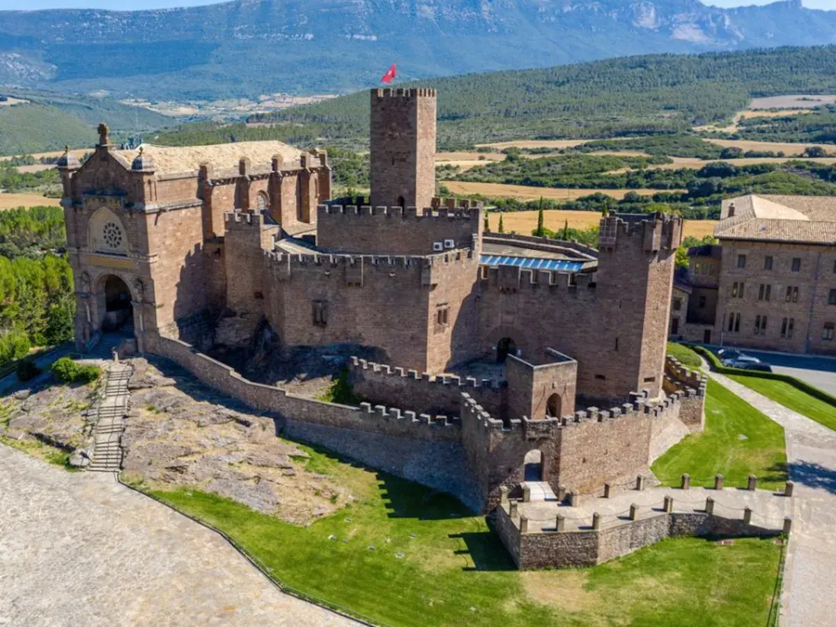 Imponente castillo de Javier, con su basílica anexa y torres defensivas, se alza majestuoso sobre un paisaje verde y montañoso.