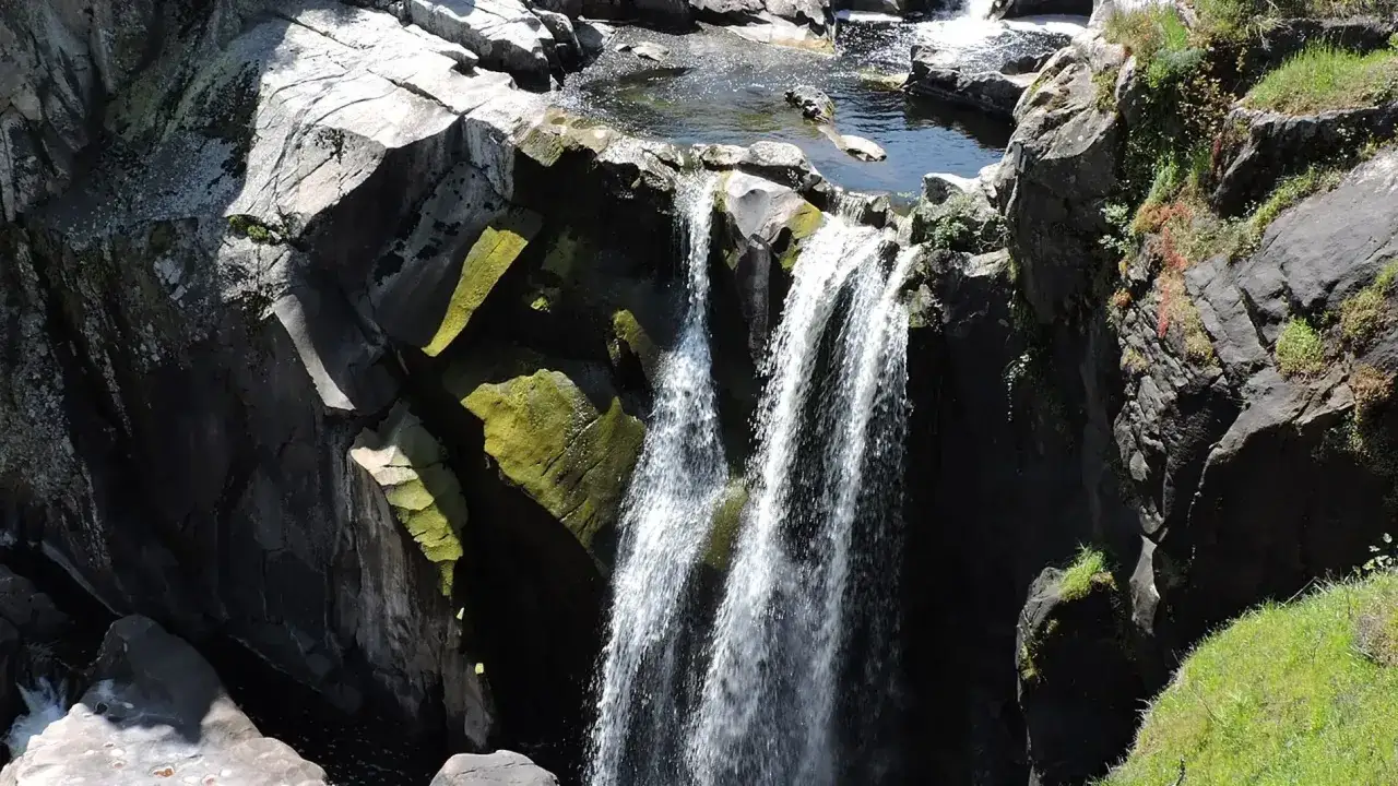Cascada en el pozo de los humos, con rocas oscuras cubiertas de musgo verde y agua cayendo en cortinas blancas.
