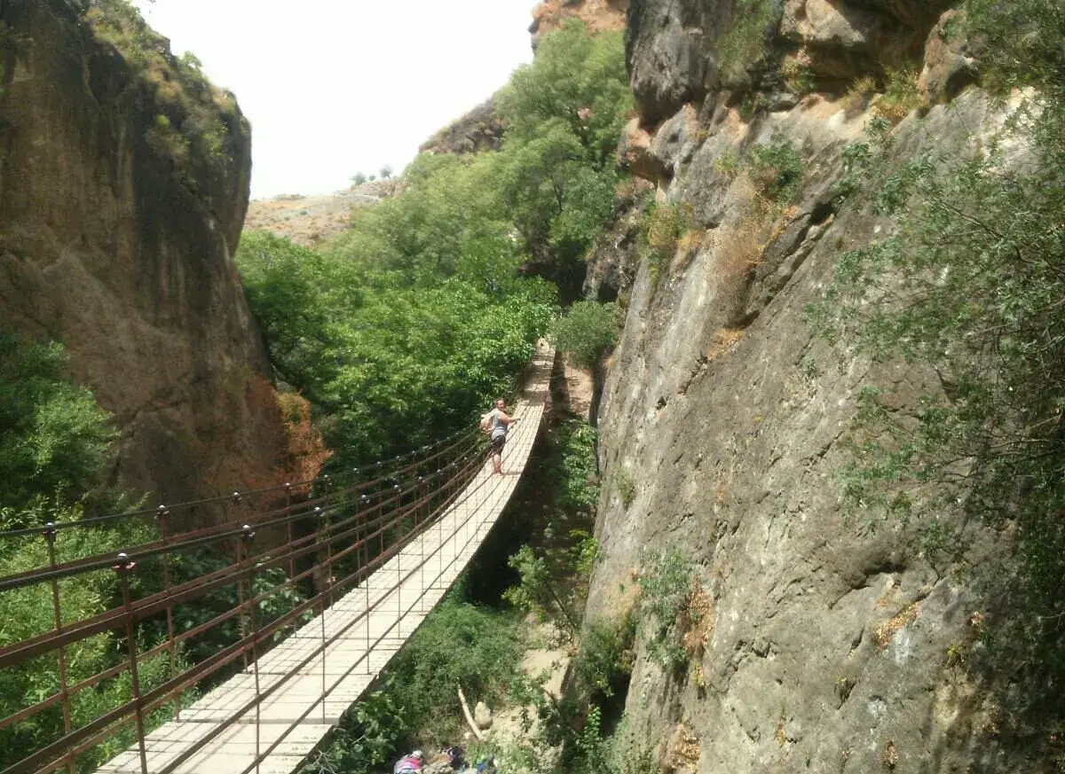 Persona camina por el puente colgante de la ruta de los Cahorros, rodeada de vegetación y acantilados.
