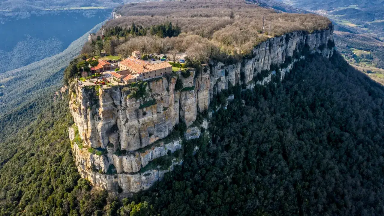 El santuari del far, un conjunto de edificios con tejados rojos, se alza majestuoso sobre un acantilado rocoso, rodeado de bosques frondosos.