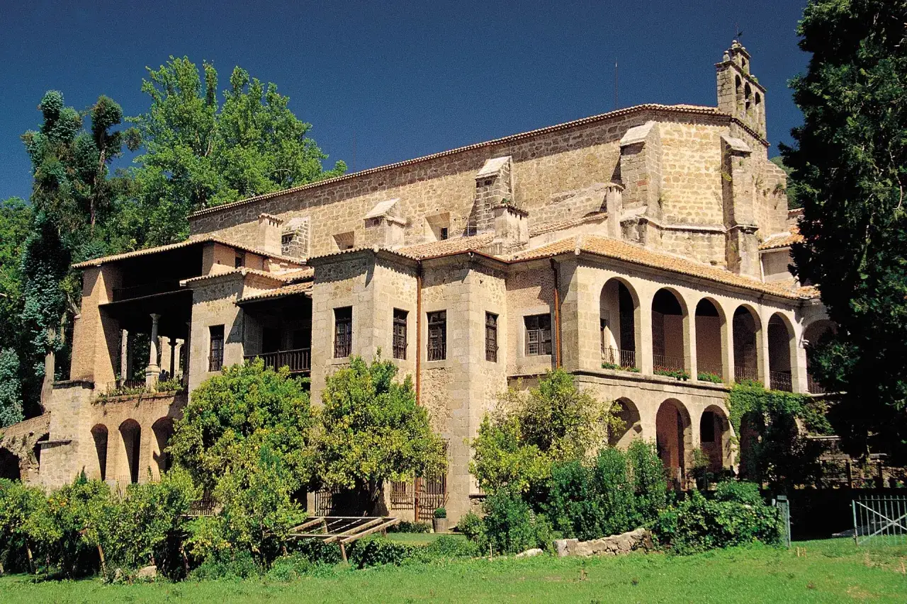 Monasterio de Yuste, con sus arcos y tejados, rodeado de vegetación exuberante. Un lugar histórico donde el emperador Carlos V pasó sus últimos años.