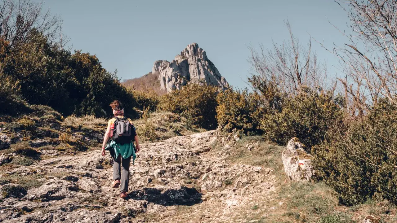 Senderista asciende por un camino rocoso hacia un pico montañoso, disfrutando de las rutas por Burgos.