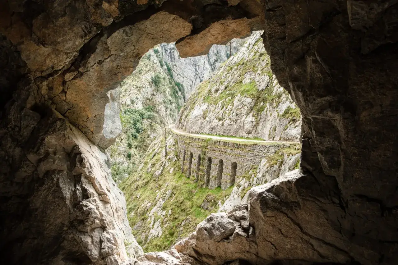 Vista desde una cueva de la ruta del Cares, con un camino tallado en la roca y arcos de piedra. El tiempo parece perfecto para la aventura.