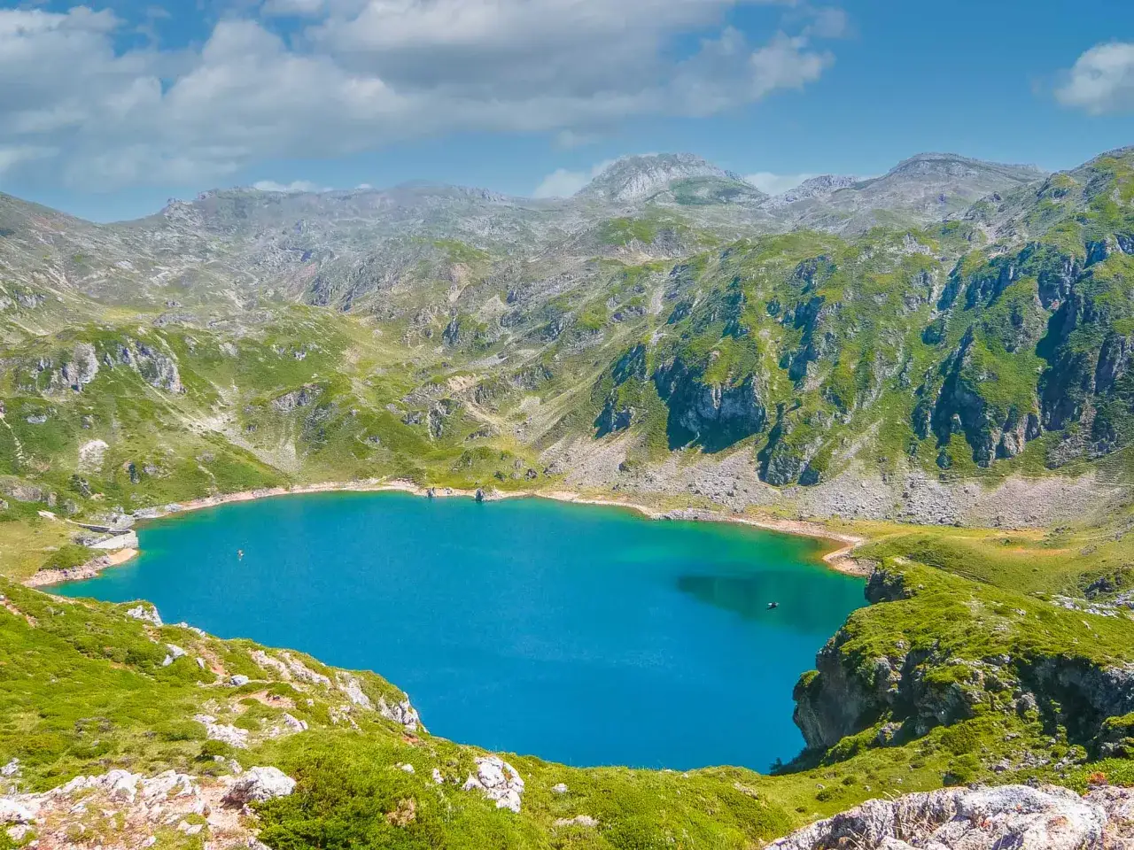 Impresionante vista de la ruta Lagos de Saliencia, con un lago azul turquesa rodeado de montañas verdes y rocosas bajo un cielo nublado.