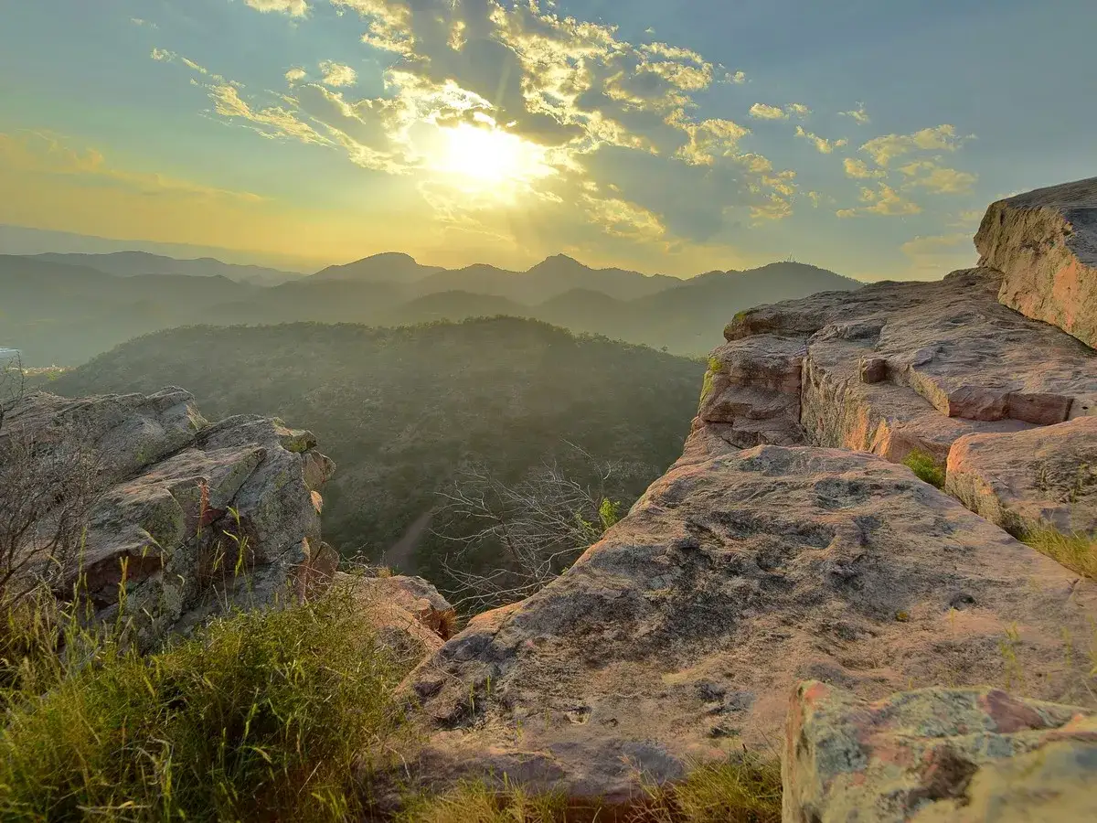 Atardecer sobre las montañas, ideal para rutas senderismo Castellón. Rocas rojizas y vegetación en primer plano.