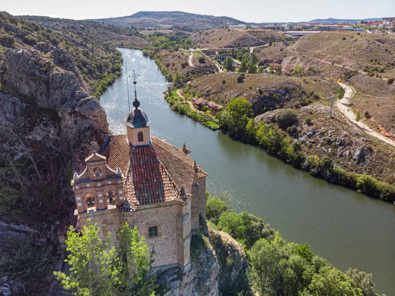 Ermita de San Saturio, Soria, junto al río Duero, con un paisaje de colinas y vegetación.