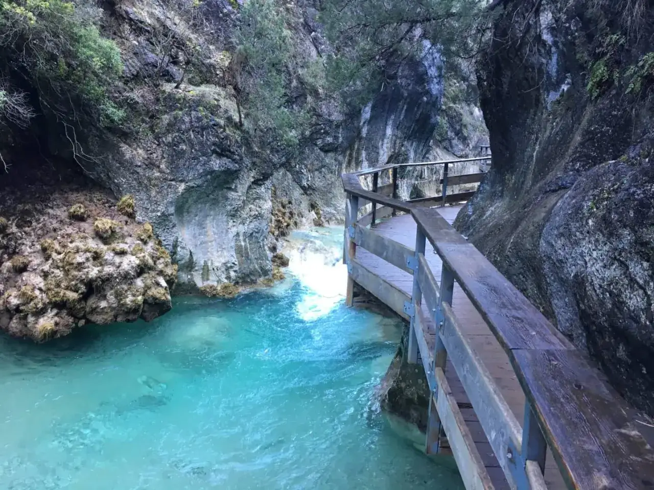 Pasarela de madera junto a un r&iacute;o turquesa en la cerrada de El&iacute;as. Rocas escarpadas y vegetaci&oacute;n cubren las paredes del ca&ntilde;&oacute;n.