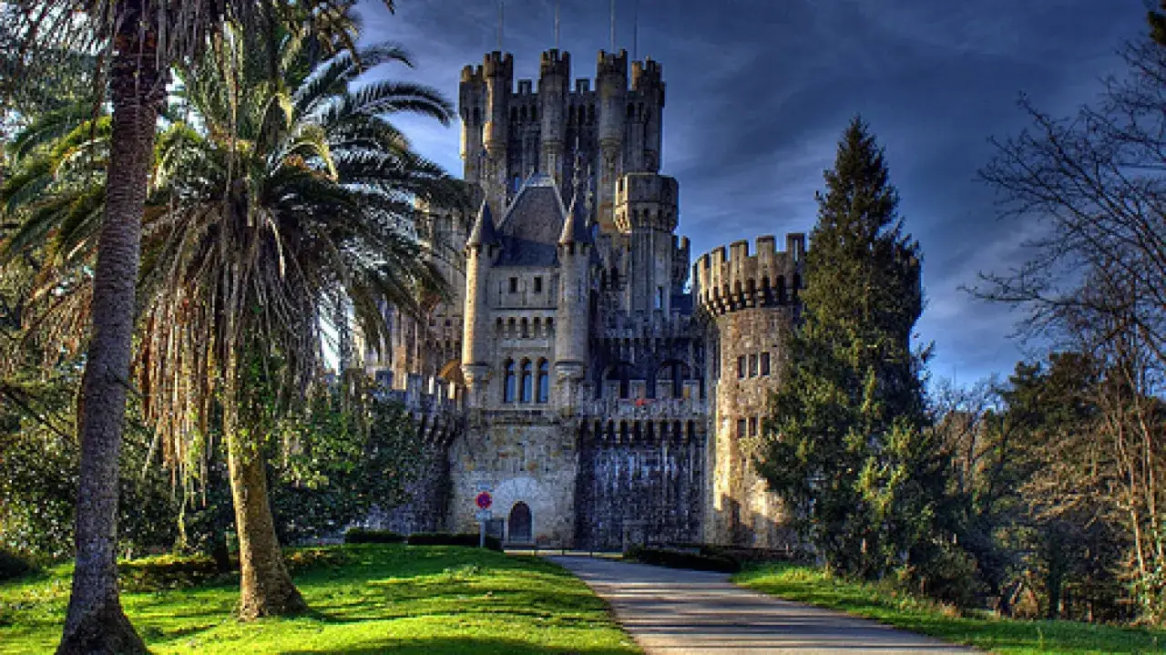 Majestuoso castillo de Butrón, con sus torres y almenas, rodeado de palmeras y vegetación exuberante bajo un cielo azul.