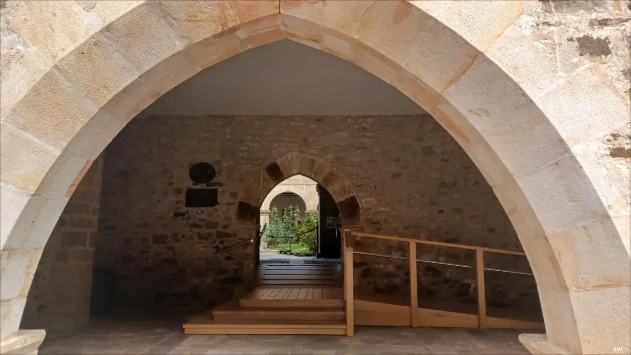 Arco de piedra en el Monasterio de Santo Toribio de Liébana, con pasarela de madera y jardín al fondo.