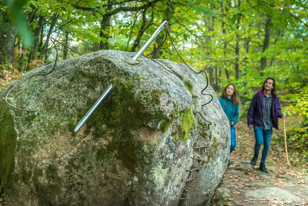 Un par explora el bosque de los espejos, admirando una roca cubierta de musgo con varillas metálicas que parecen agujas.