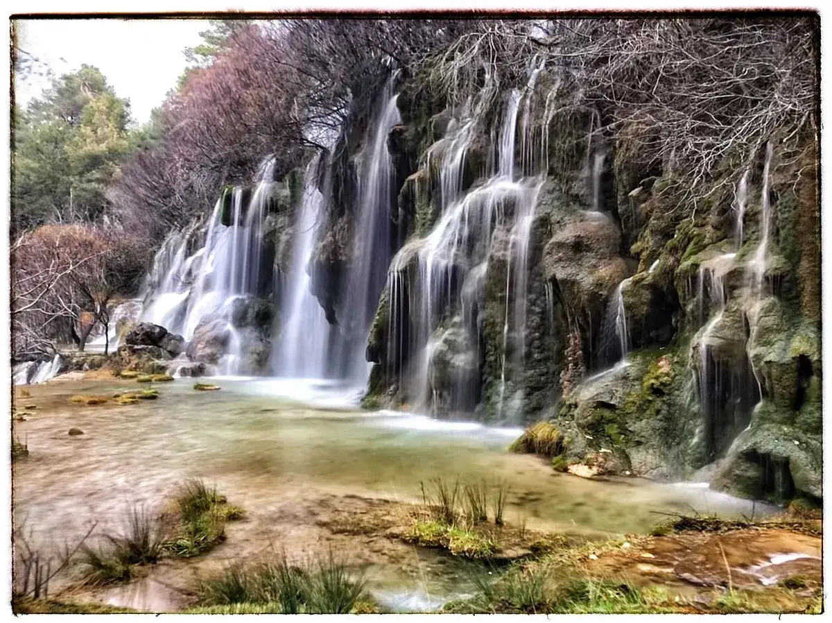 Cascada en la ruta nacimiento río Cuervo. El agua cae en velos sobre rocas cubiertas de musgo, creando un paisaje sereno.