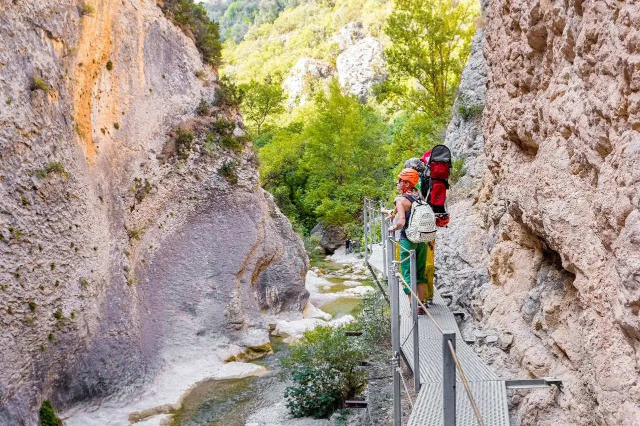 Dos excursionistas disfrutan de las pasarelas de Alquézar, un sendero metálico junto a un río y paredes rocosas.