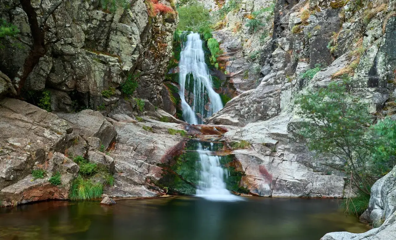 Cascada del Purgatorio, una ruta natural con agua cayendo entre rocas cubiertas de musgo y vegetación.