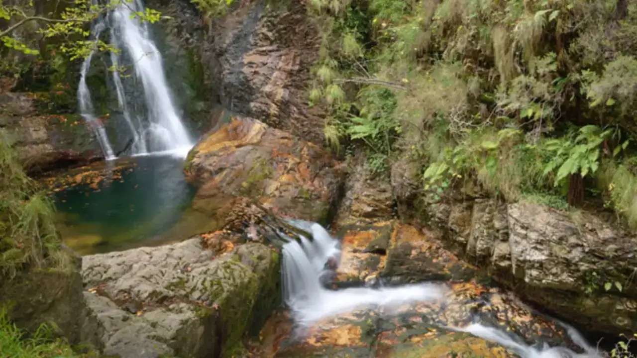 Cascada en la ruta del alba, con agua cayendo sobre rocas y vegetaci&oacute;n exuberante.
