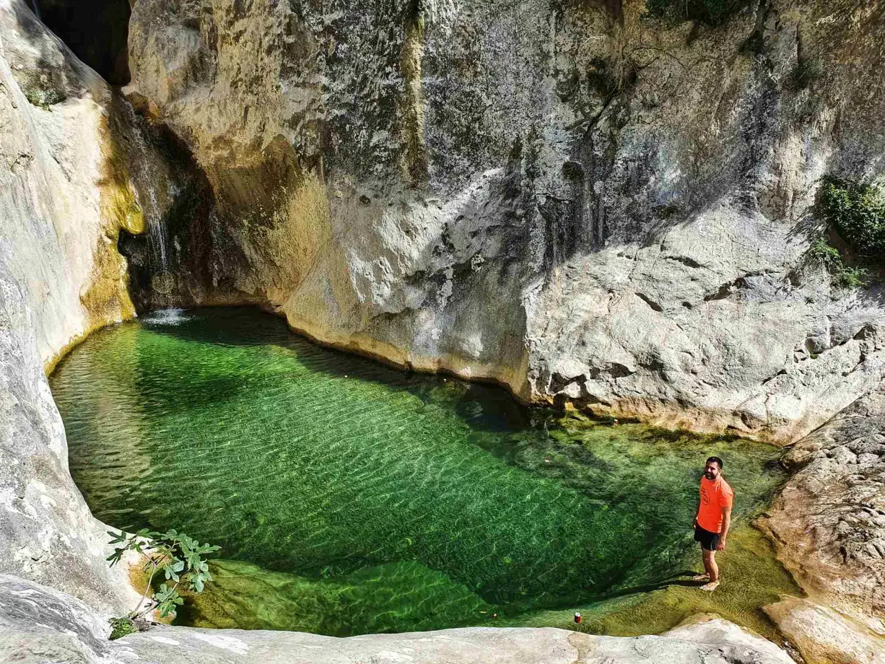 Un hombre se baña en el gorg blau Girona, un oasis de aguas cristalinas rodeado de rocas y vegetación.