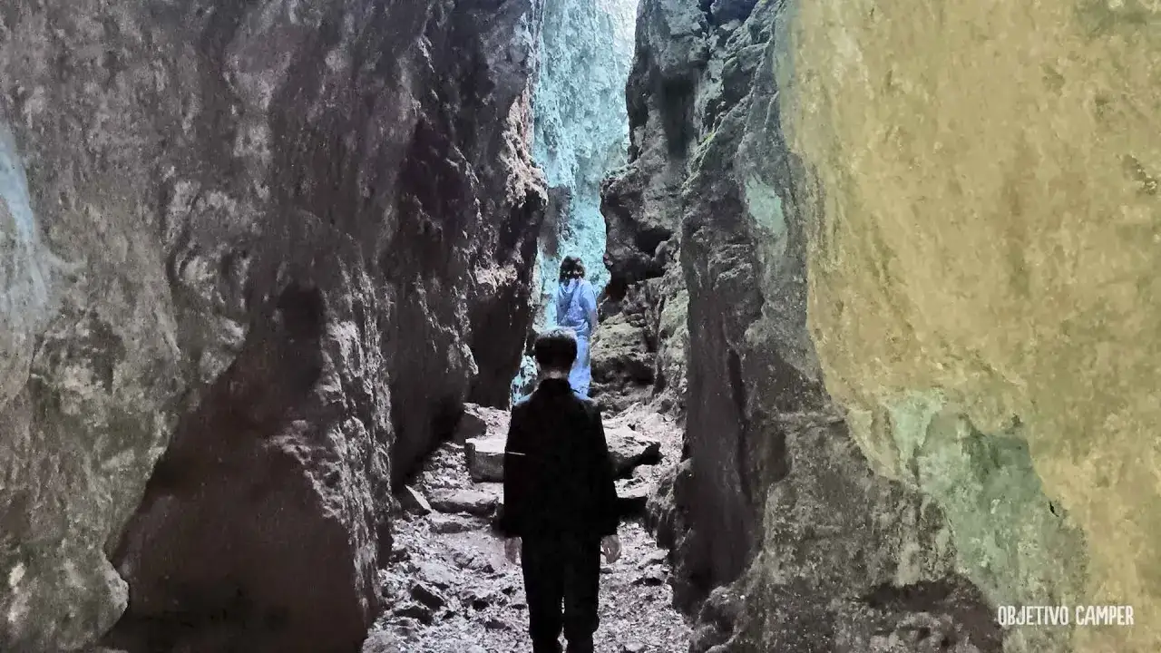 Dos personas caminan por un estrecho sendero entre imponentes paredes rocosas, adentrándose en los avencs de la Febró.