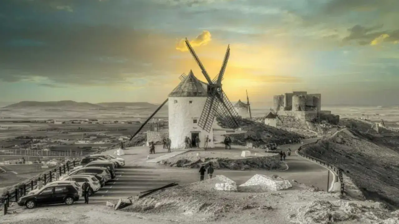 Los icónicos molinos de Consuegra se alzan majestuosos bajo un cielo dramático, con un castillo al fondo.