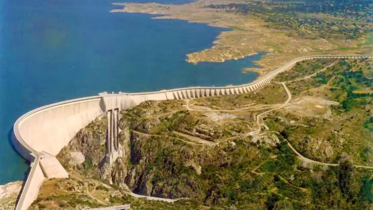 La imponente presa de Almendra, una obra de ingenier&iacute;a que retiene un vasto embalse azul, se alza majestuosa entre colinas rocosas y vegetaci&oacute;n.