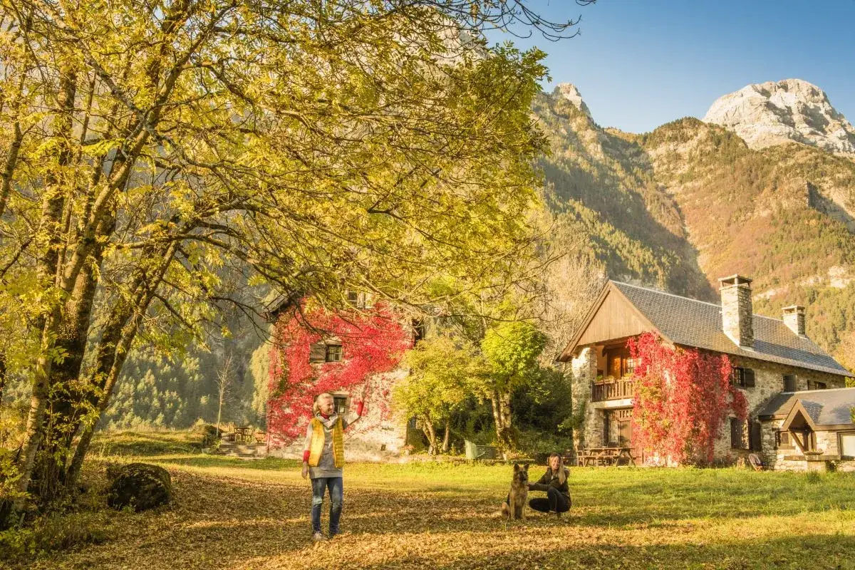 Dos mujeres y un perro disfrutan de un d&iacute;a oto&ntilde;al en el valle de Pineta, ideal para rutas. Las casas cubiertas de hiedra roja y las monta&ntilde;as imponentes crean un paisaje espectacular.
