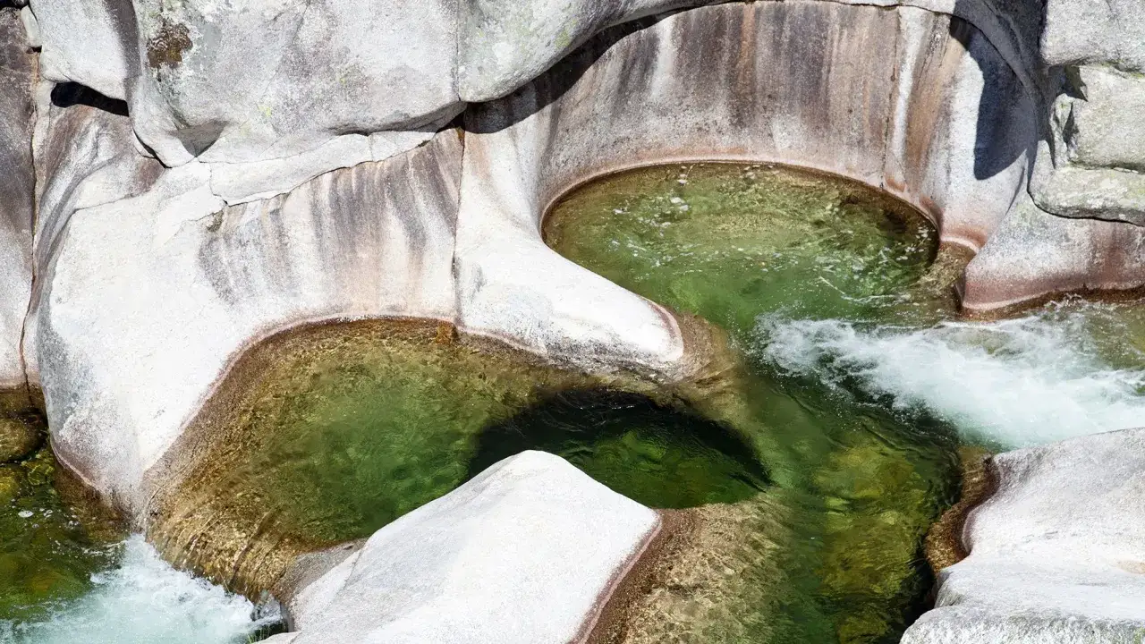 Agua verde y cristalina fluye entre rocas erosionadas, formando pozas naturales en la Garganta de los Infiernos.