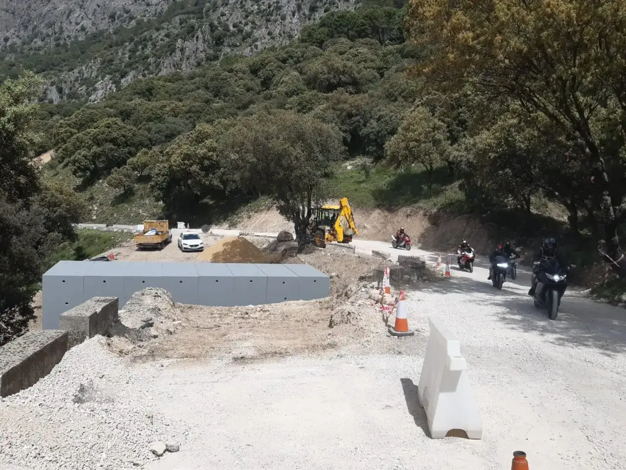 Motociclistas se acercan a Benamahoma por una carretera en obras, con maquinaria y materiales de construcción.
