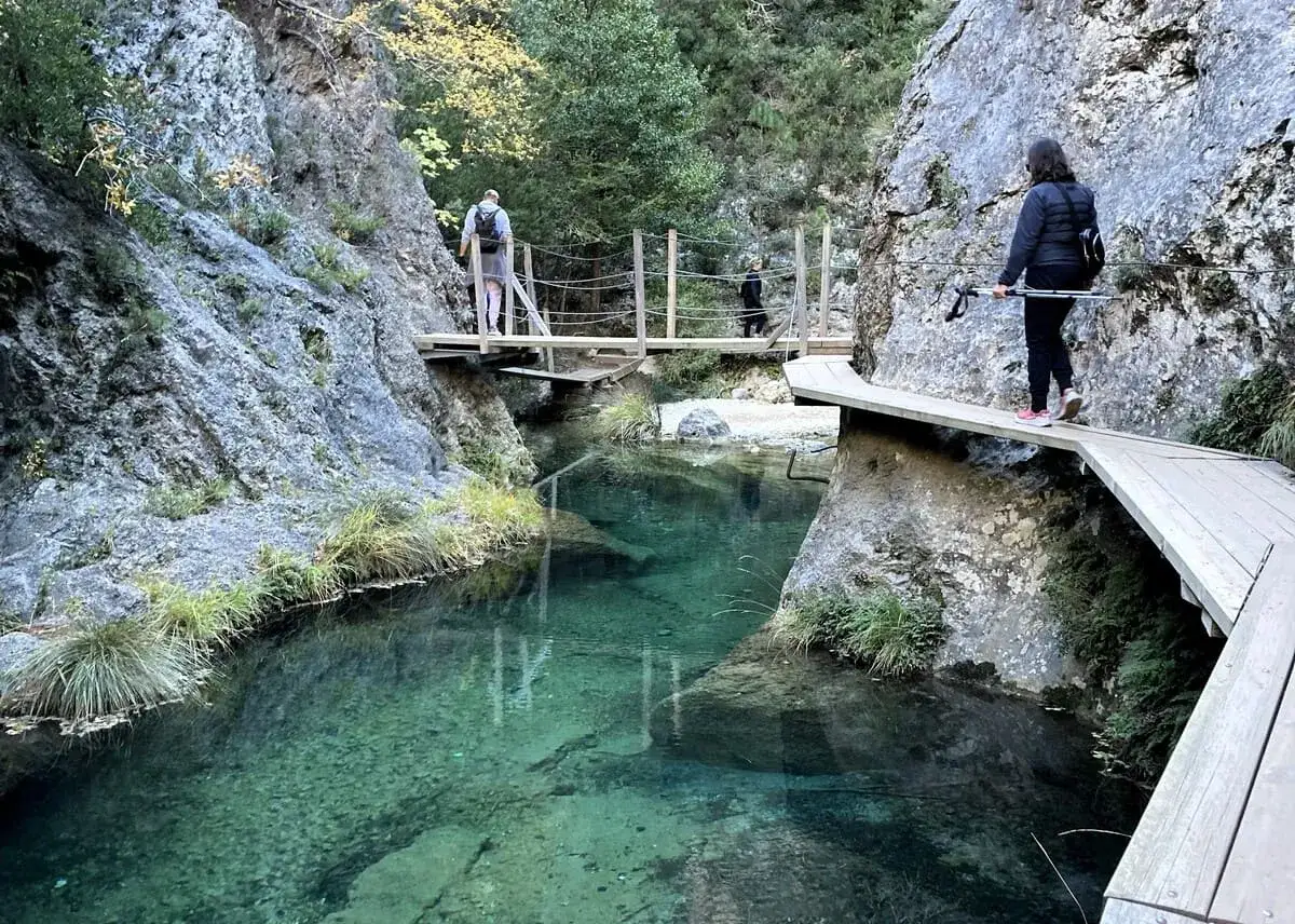 Senderistas disfrutan del Parrizal de Beceite, con sus pasarelas de madera sobre aguas cristalinas y rocas escarpadas.