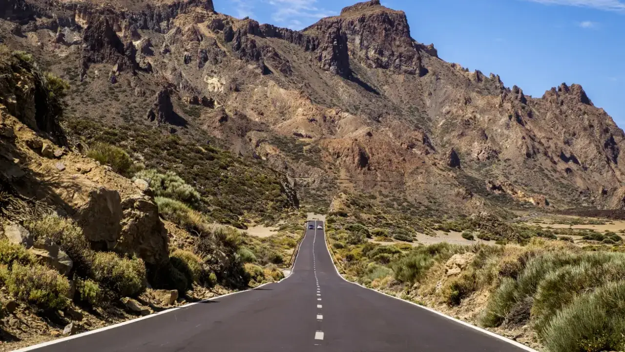 Carretera ascendente hacia el Teide, rodeada de vegetación volcánica y rocas. Un viaje escénico para subir al Teide en coche.