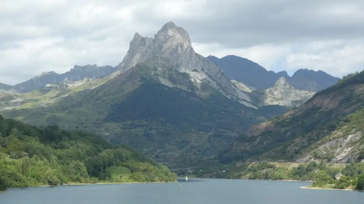 Majestuoso pico rocoso en un valle verde con un lago azul. Para llegar a Lanuza, sigue el camino serpenteante.