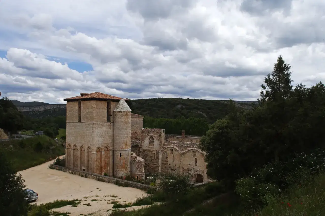 Ruinas del monasterio de San Pedro de Arlanza, con su torre robusta y arcos de piedra bajo un cielo nublado.