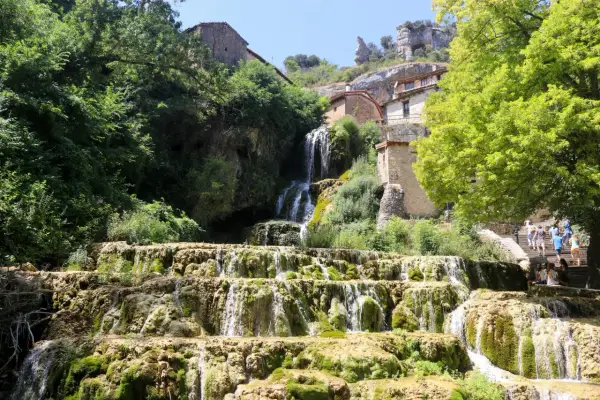 Cascada en las Hoces del Ebro, con casas de piedra integradas en la roca y vegetación exuberante.